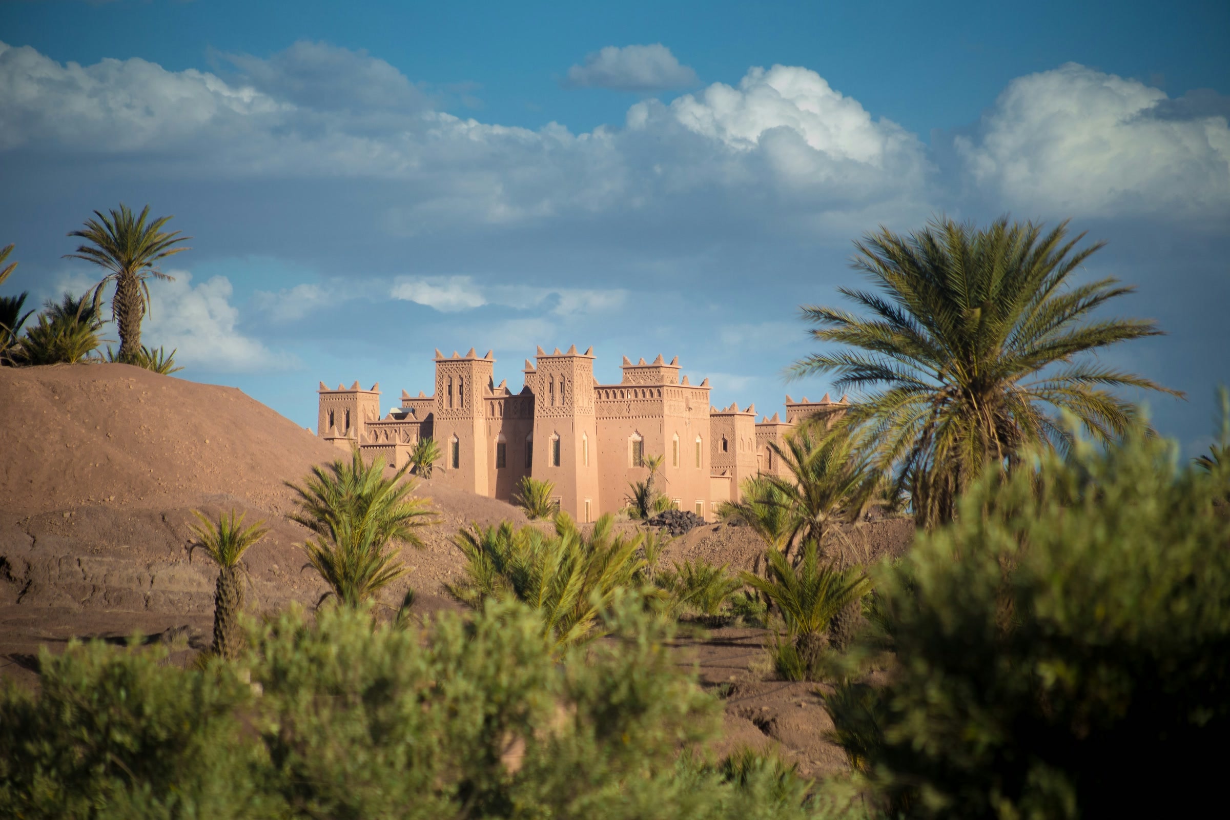 A sunlit earthen kasbah framed by date palms beneath a blue sky