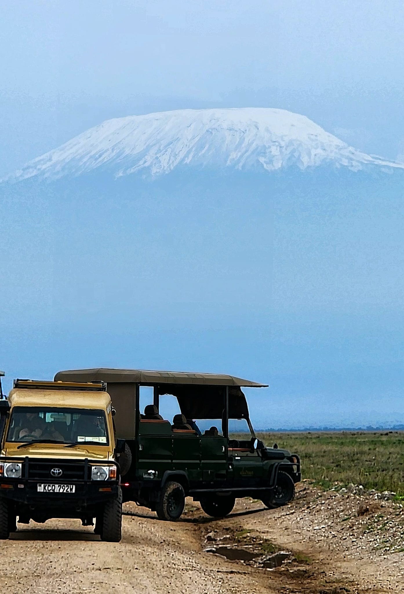 Safari vehicles on a track beneath snow-capped Kilimanjaro