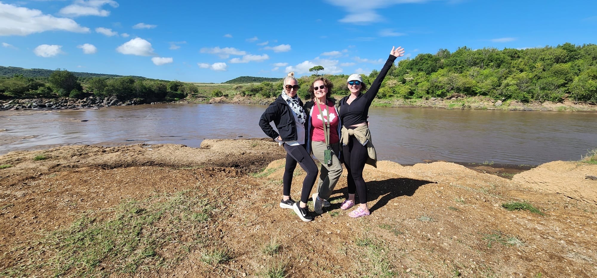 Three friends posing by a river on safari